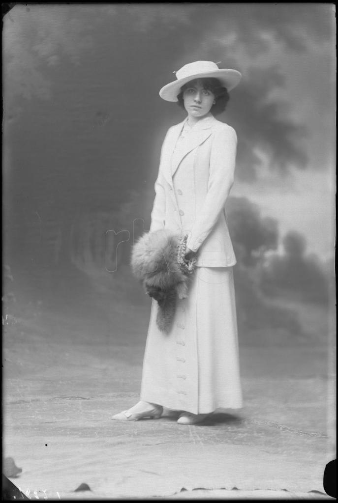 MIMI ESTAMPES CON UN TRAJE BLANCO, UN SOMBRERO Y UN MANGUITO