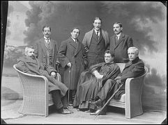 SACERDOTE SENTADO CON SEIS HOMBRES