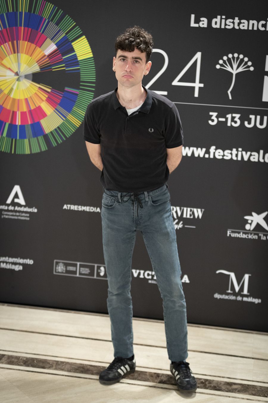 Álex Monner lleva vaqueros con un polo negro y deportivas Adidas