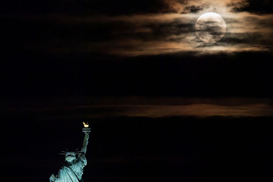 La primera luna llena del verano asoma por detrás de la estatua de la libertad de Nueva York