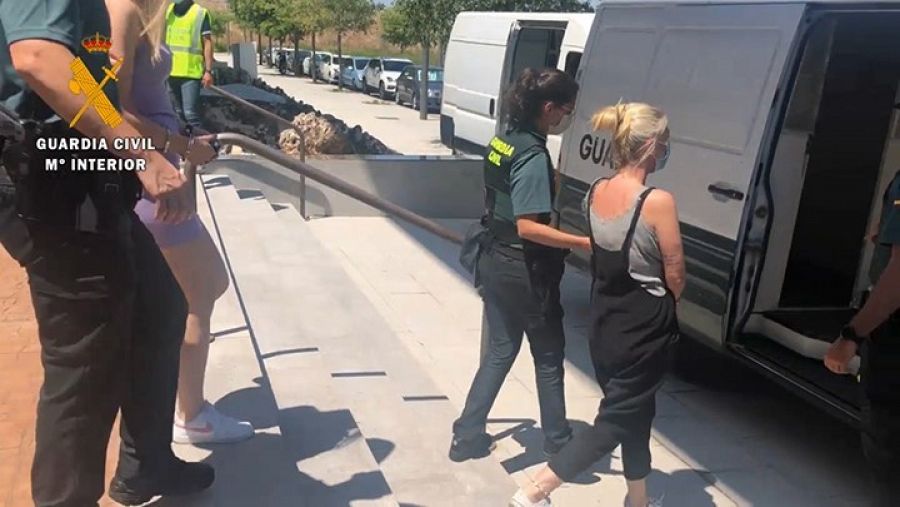 Dos mujeres detenidas por la Guardia Civil caminan esposadas hacia un vehículo policial.