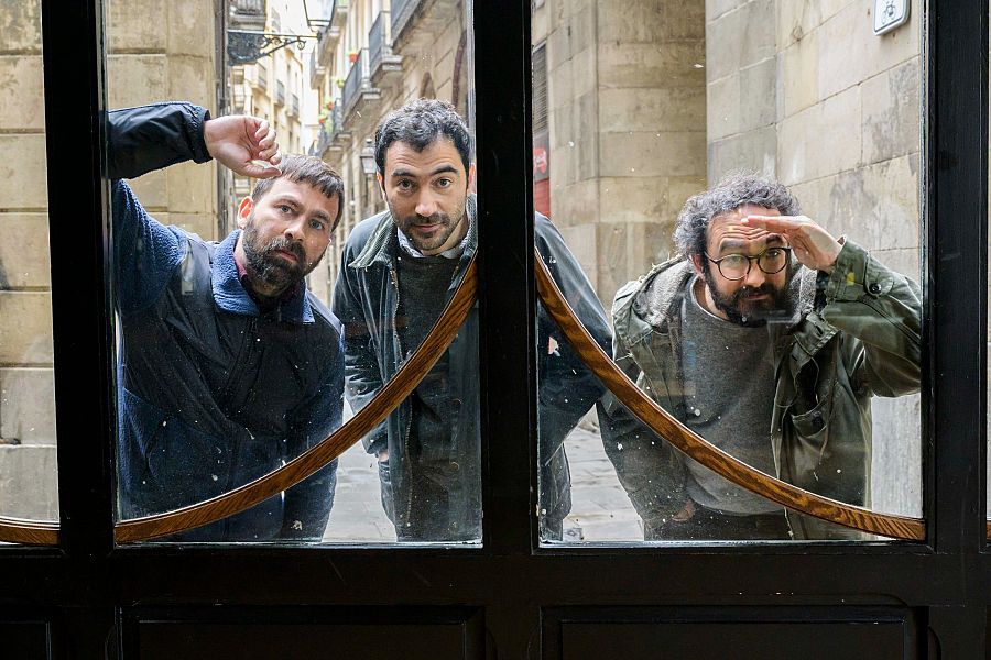 Els tres membres de Mujeres mirant a través del vidre d'una porta