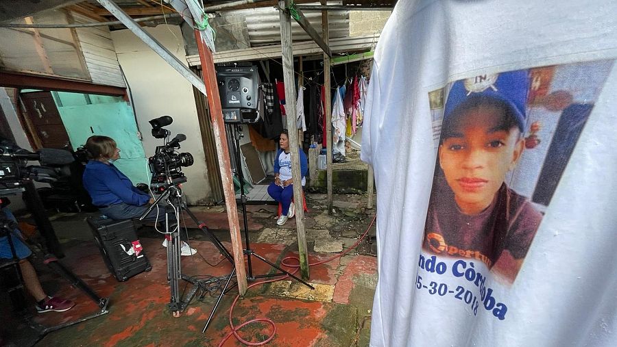 Camiseta en primer plano con el retrato de un estudiante asesinado y, en el fondo, su madre entrevistada por RTVE.
