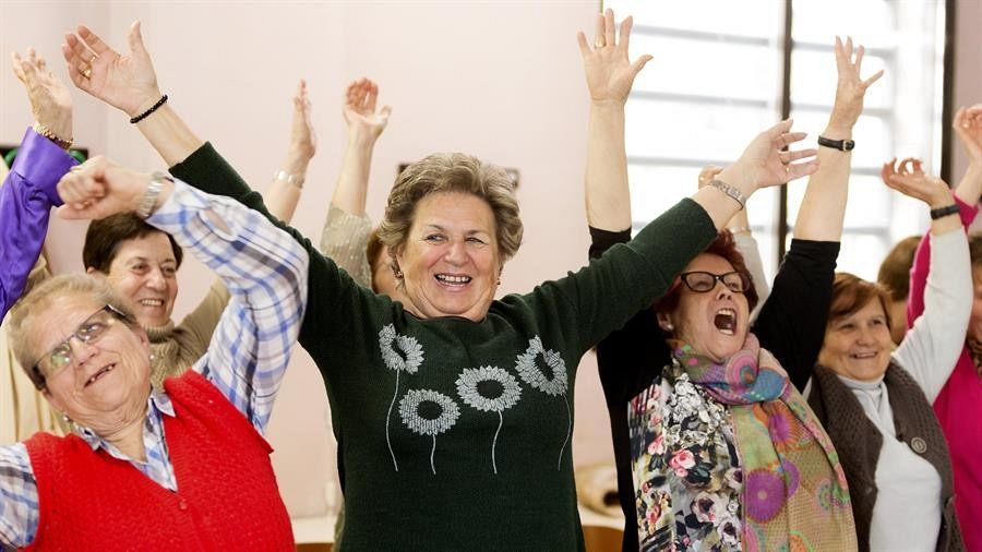 Un grupo de mujeres mayores se ríe con los brazos en alto.