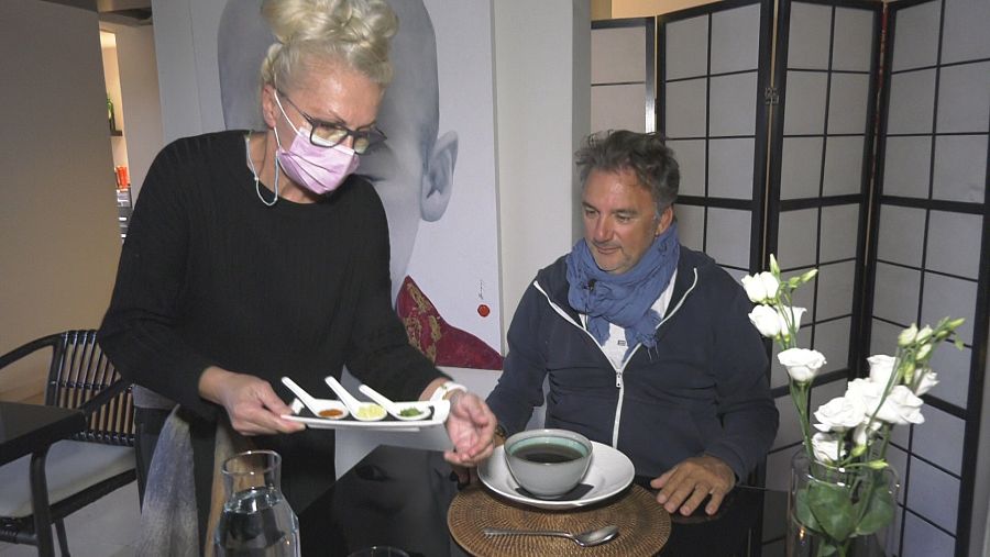 Una camarera sirve zumos y caldos a un comensal.