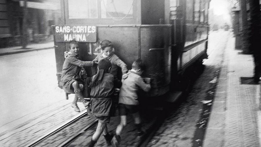 Uns nens s'enfilen de manera perillosa a un tramvia amb parades en els barris de Sants, Les Corts i Marina, datada entre 1920 i 1939