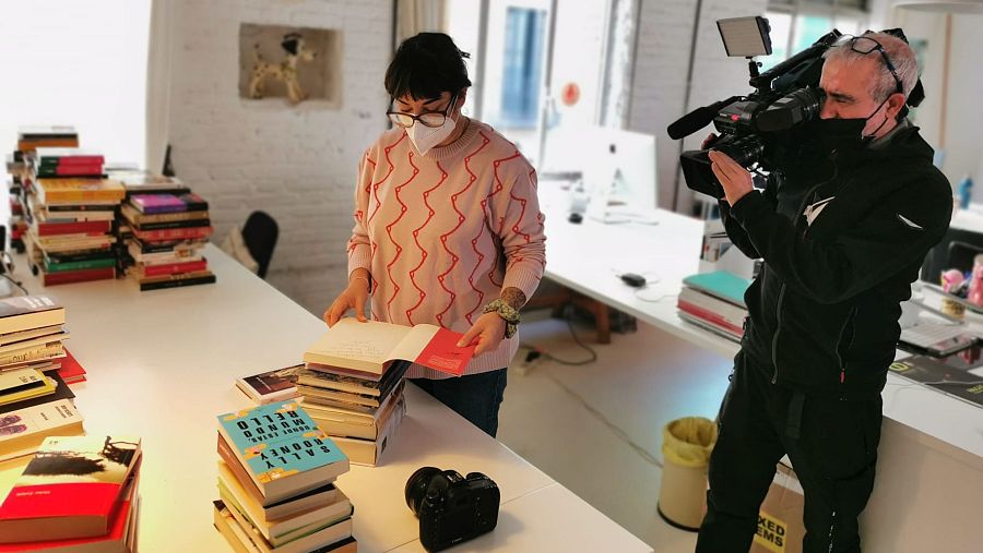 Un reportero de TVE graba a una voluntaria junto a un montón de libros dedicados.