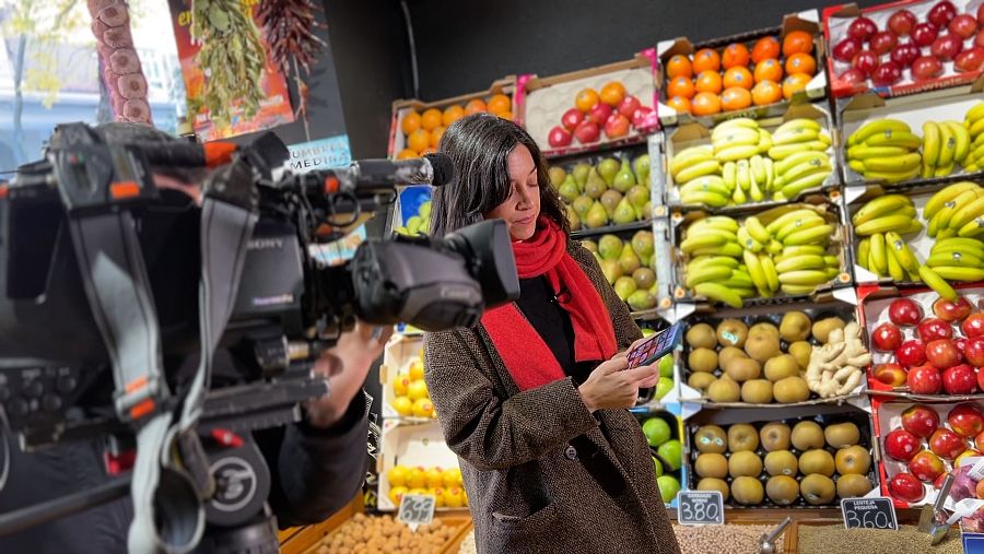 La historiadora del arte Blanca Serrano mira su móvil frente a una frutería con plátanos.