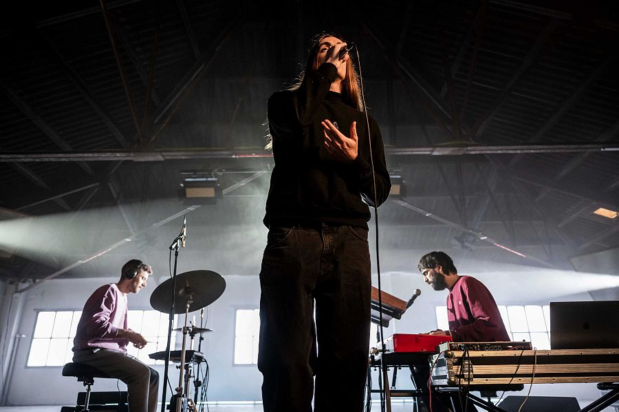 En primer pla Phoac cantant amb micro i darrere b1n0 amb bateria i teclat