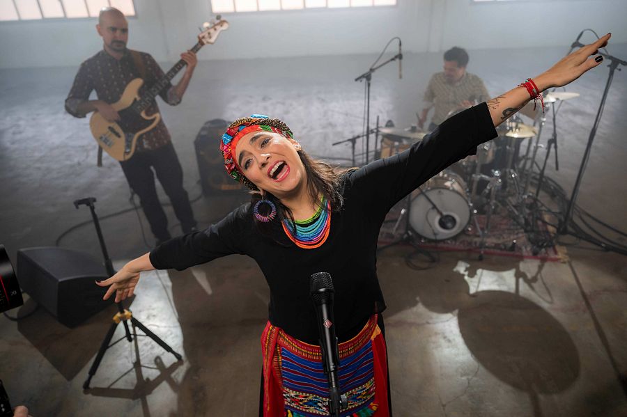 Marta Gómez en un moment de l'actuació amb els braços oberts i el bateria i el guitarrista que l'acompanyen darrere