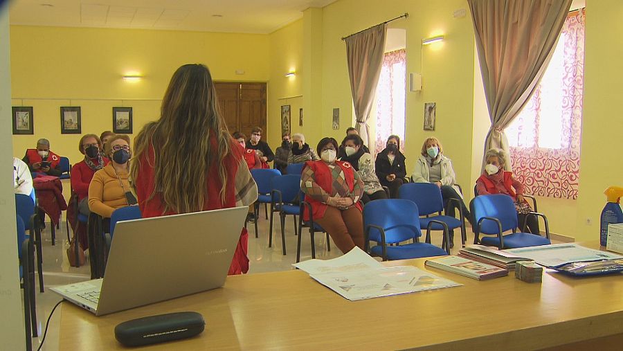 Clase con profesora de Cruz Roja de espaldas y alumnas atendiendo sentadas.
