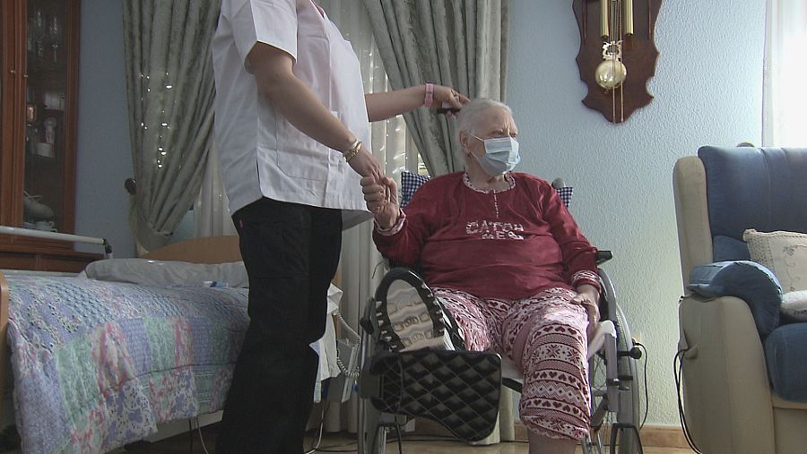 Una mujer en silla de ruedas coge la mano de su cuidadora.