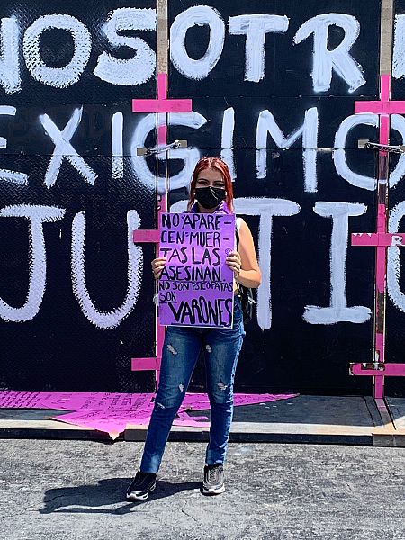 Naila posa sujetando una pancarta morada en México