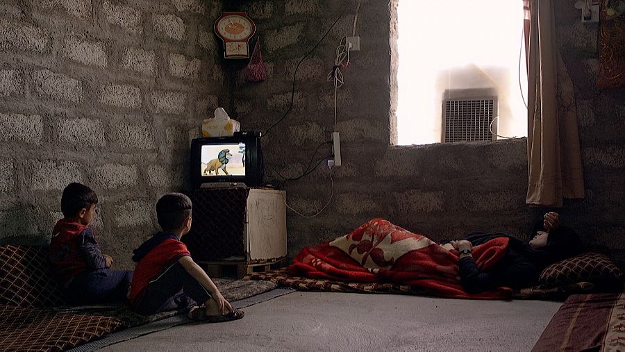 Imad y su hemano ven la televisión mientras su madre está tumbada
