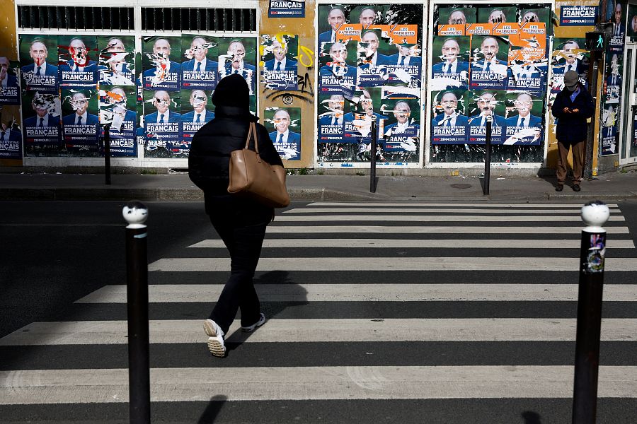 Una mujer cruza un paso de cebra hacia una pared empapelada con carteles de Eric Zemmour en París.