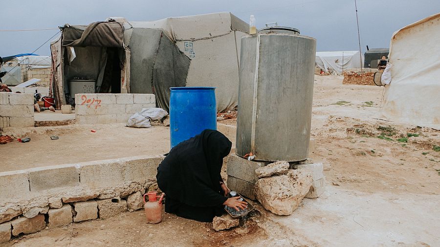 Una mujer lava los platos usando un tanque de agua en un campamento en el noroeste de Siria