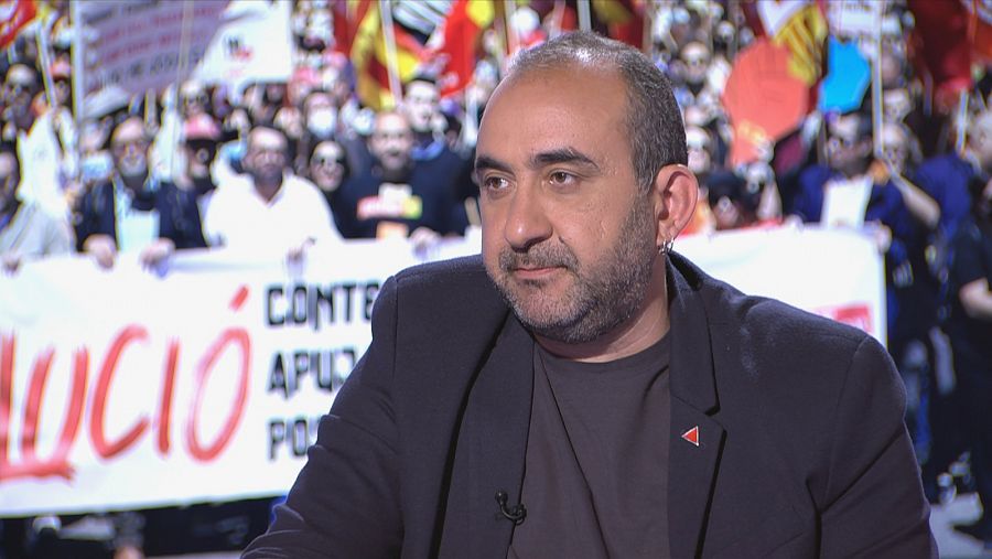 Javier Pacheco al plató del programa amb una pantalla amb vídeo de manifestació darrere