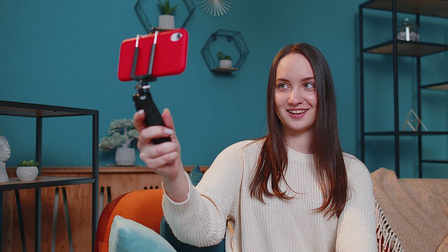 Una joven influencer se graba con el móvil en el salón de su casa.