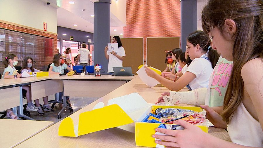 Un grupo de niñas abren cajas de cartón amarillo que contienen piezas de Lego.