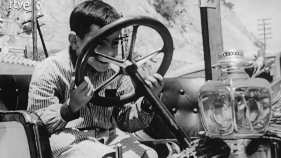 Un infant fa veure que condueix a un cotxe antic aparcat, abans de començar el ral·li del Gran Premi Costa Brava del 1962