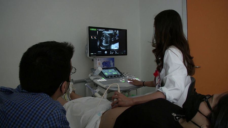 Ecografía de mujer embarazada con la asistencia de su pareja y del sanitario.
