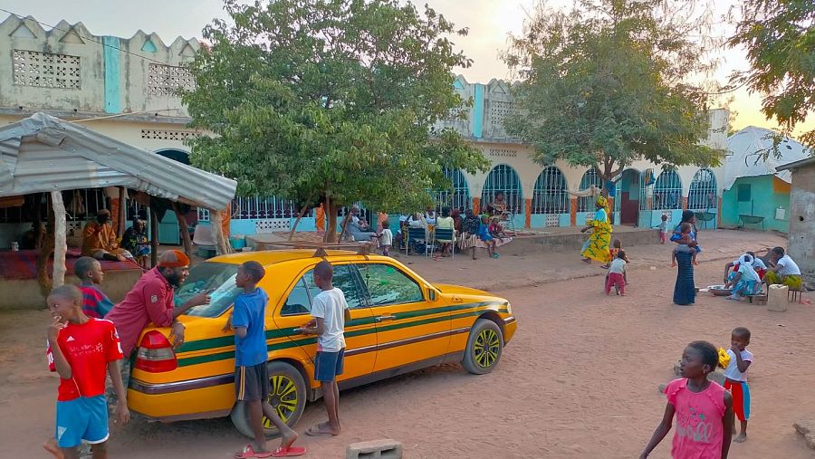 Salim en su aldea con niños de su familia rodeando su taxi