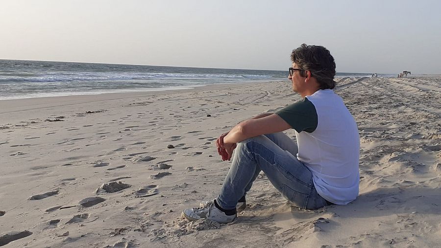 Hombre mirando al mar sentado en la arena de una playa en Mauritania