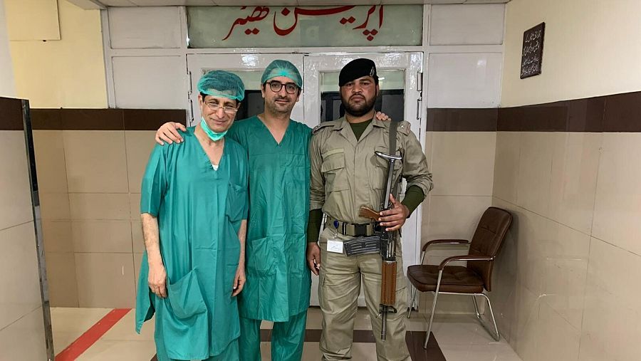 Dos cirujanos vestidos para operar y un soldado con metralleta