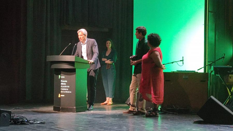 Oriol Nolis recull el premi Alícia parlant a l'atril, acompanyat de Gonzalo Bello i Consol Saenz