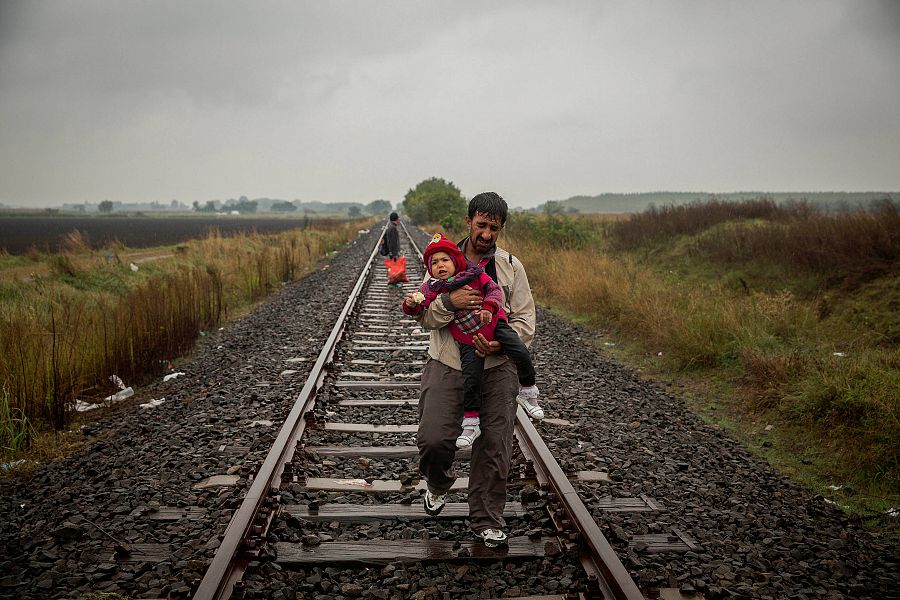 Un padre camina por las vías del tren llevando a su hijo en brazos, después de haber cruzado la frontera entre Serbia y Hungría (2015)