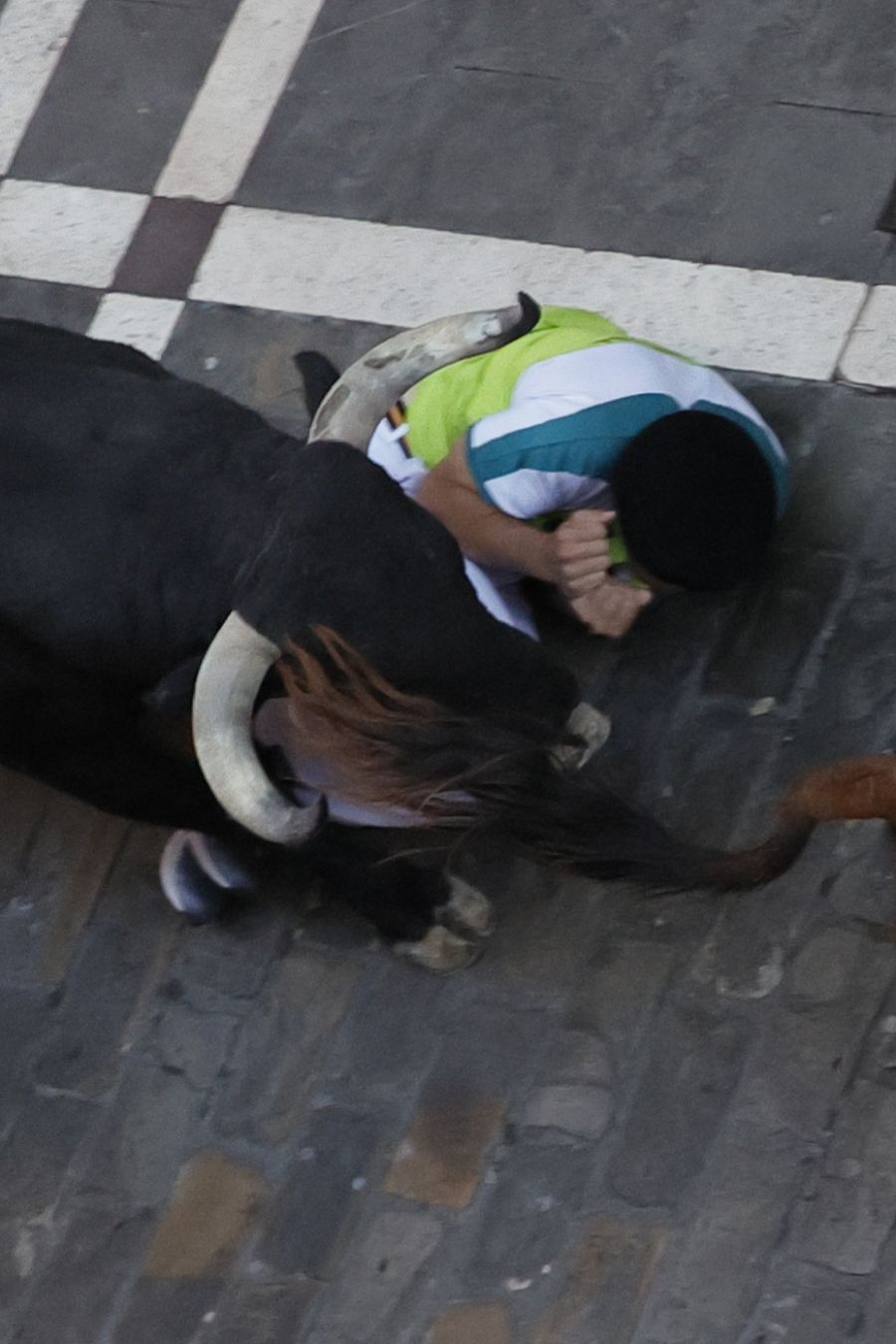 Un toro pasa por encima de dos mozos a su paso por la calle de la Estafeta.