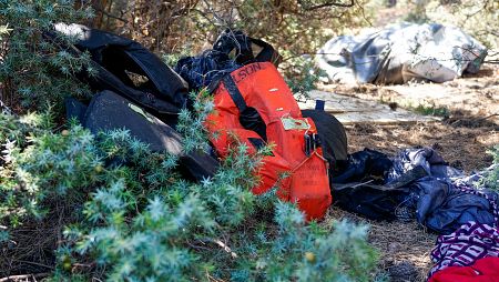 Plano medio de ropa y chalecos salvavidas de personas recién llegadas por mar a la isla de Samos, Grecia.