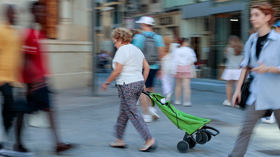 Una señora con un carro de la compra por la calle y el resto borroso.