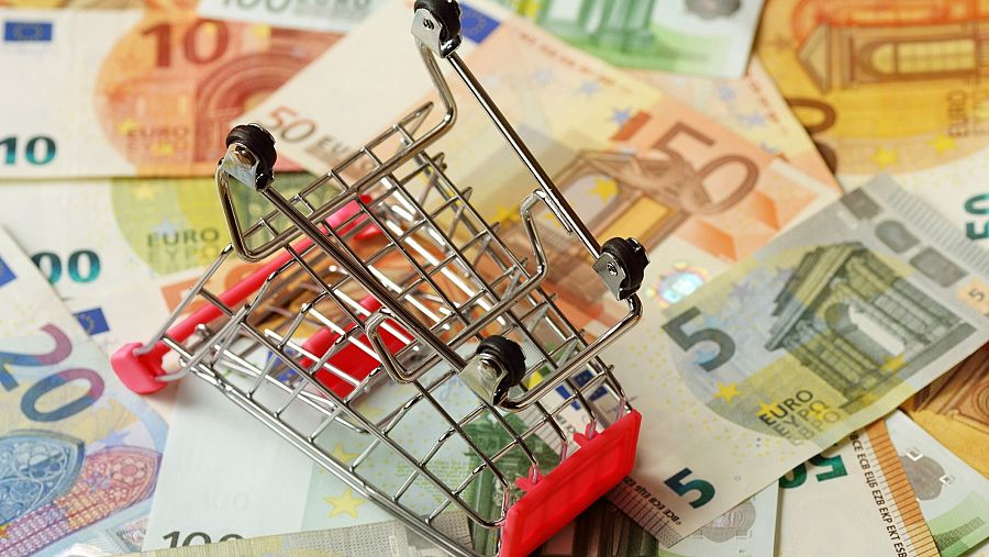 Un carrito de la compra volcado sobre billetes de euro.