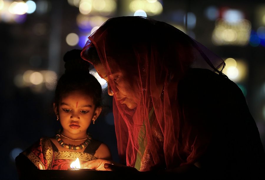 Imagen de la celebración del Diwali 2022 en Bangalore, India. Una mujer y una niña junto a una vela.