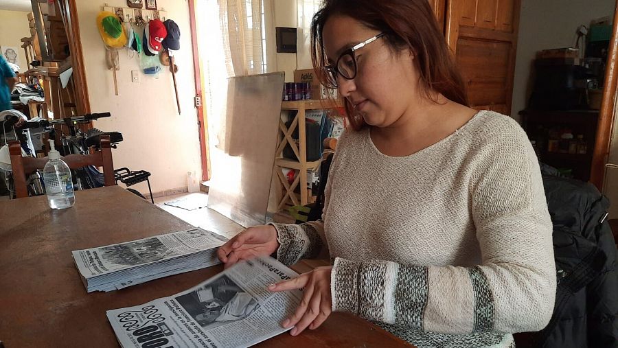 Priscila con un periódico en la mano mirand la noticia del asesinato de su padre