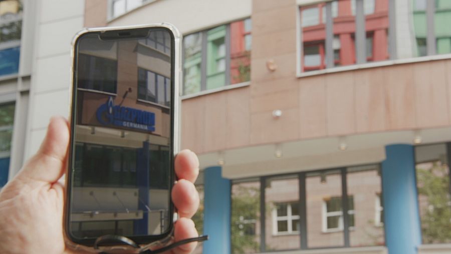 Un móvil muestra la foto con cartel de Gazprom mientras de fondo se ve el mismo edificio sin él.