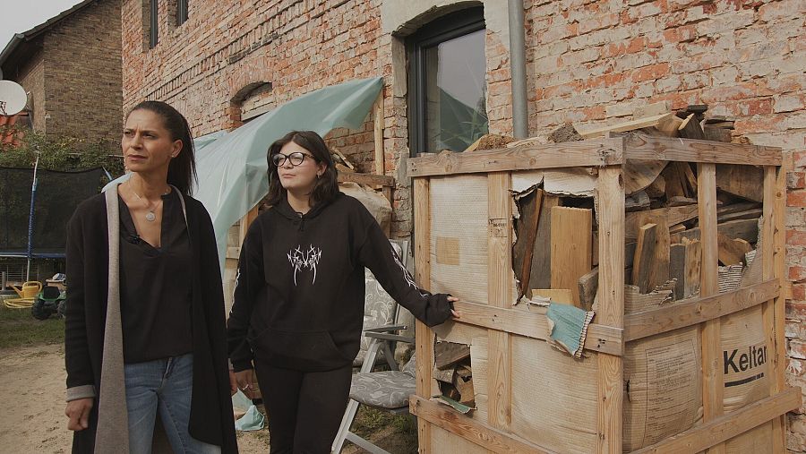 Madre e hija junto a un contenedor de maderas que usarán como combustible este invierno.