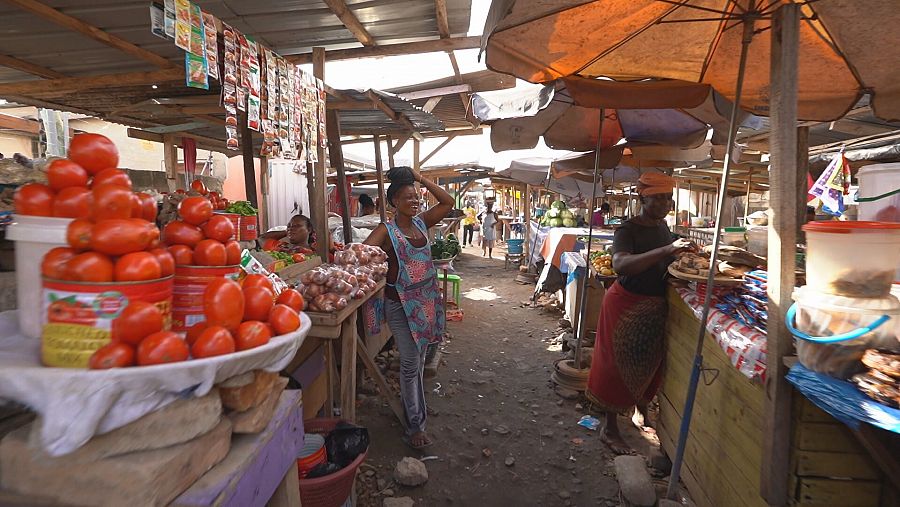 Dos mujeres conversan animadamente frente a un puesto de verduras en un mercado de Ghana.