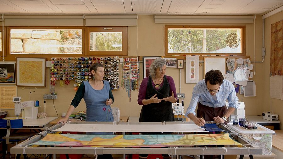 El Juan practica la pintura en seda amb les germanes González donant-li indicacions al seu taller