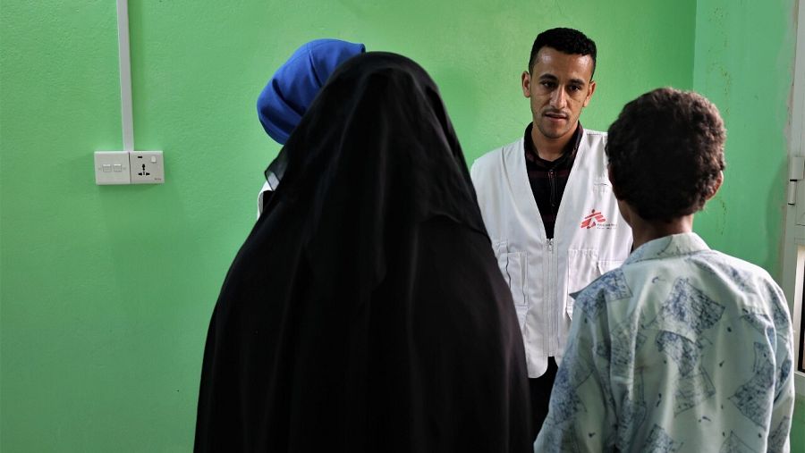 Una mujer con burka negro y su hijo, de espaldas, frente a un trabajador de MSF en Yemen