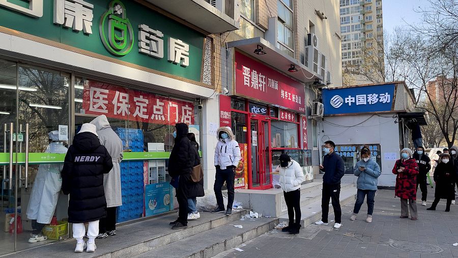 Un grupo de personas hacen cola en una farmacia de Pekín para comprar medicamentos para la COVID