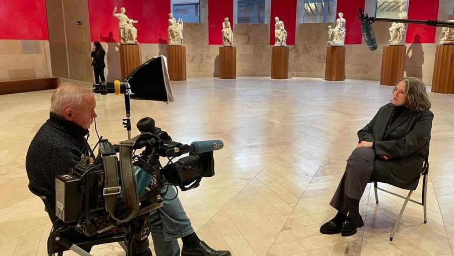 Entrevistador y entrevistada sentados en sendas sillas en una sala del Museo del Prado con esculturas clásicas de fondo.