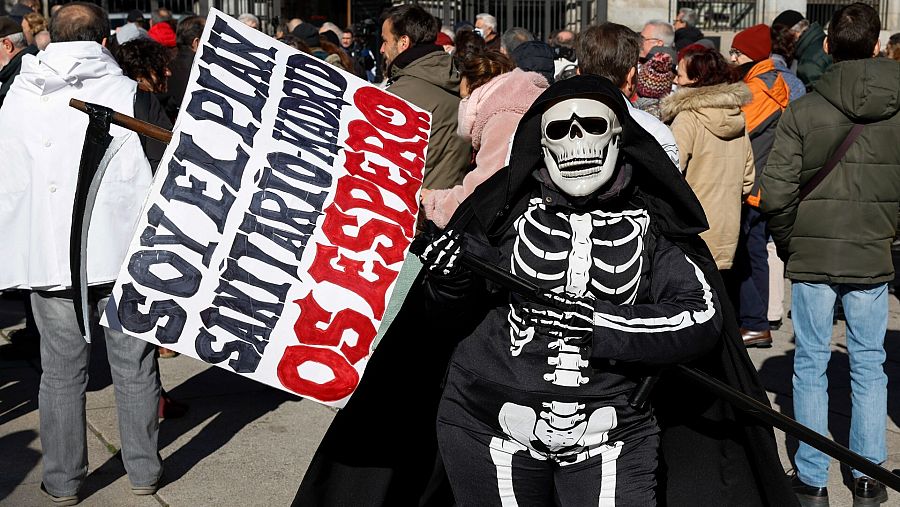 Una persona con un disfraz de esqueleto muestra una pancarta contra el plan sanitaria de Madrid.