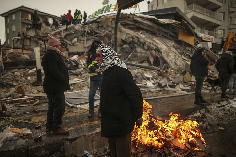 Locales se calientan al lado de un edificio destruido en Malatya después del terremoto que sacudió Turquía el pasado 6 de febrero.