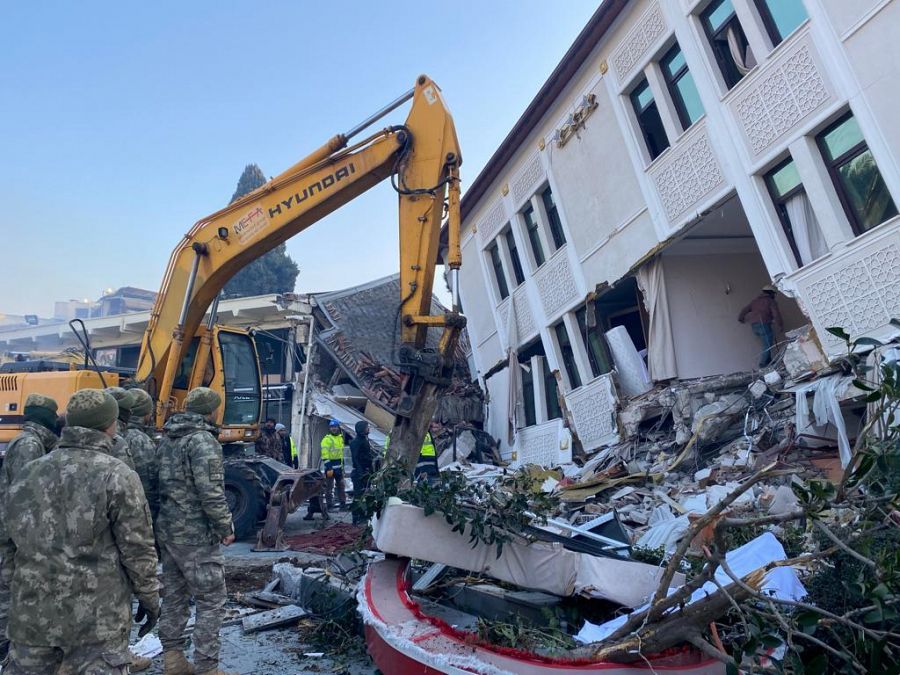 Varios militares turcos observan cómo una grúa retira los escombros de un hotel tras el terremoto en Antioquia