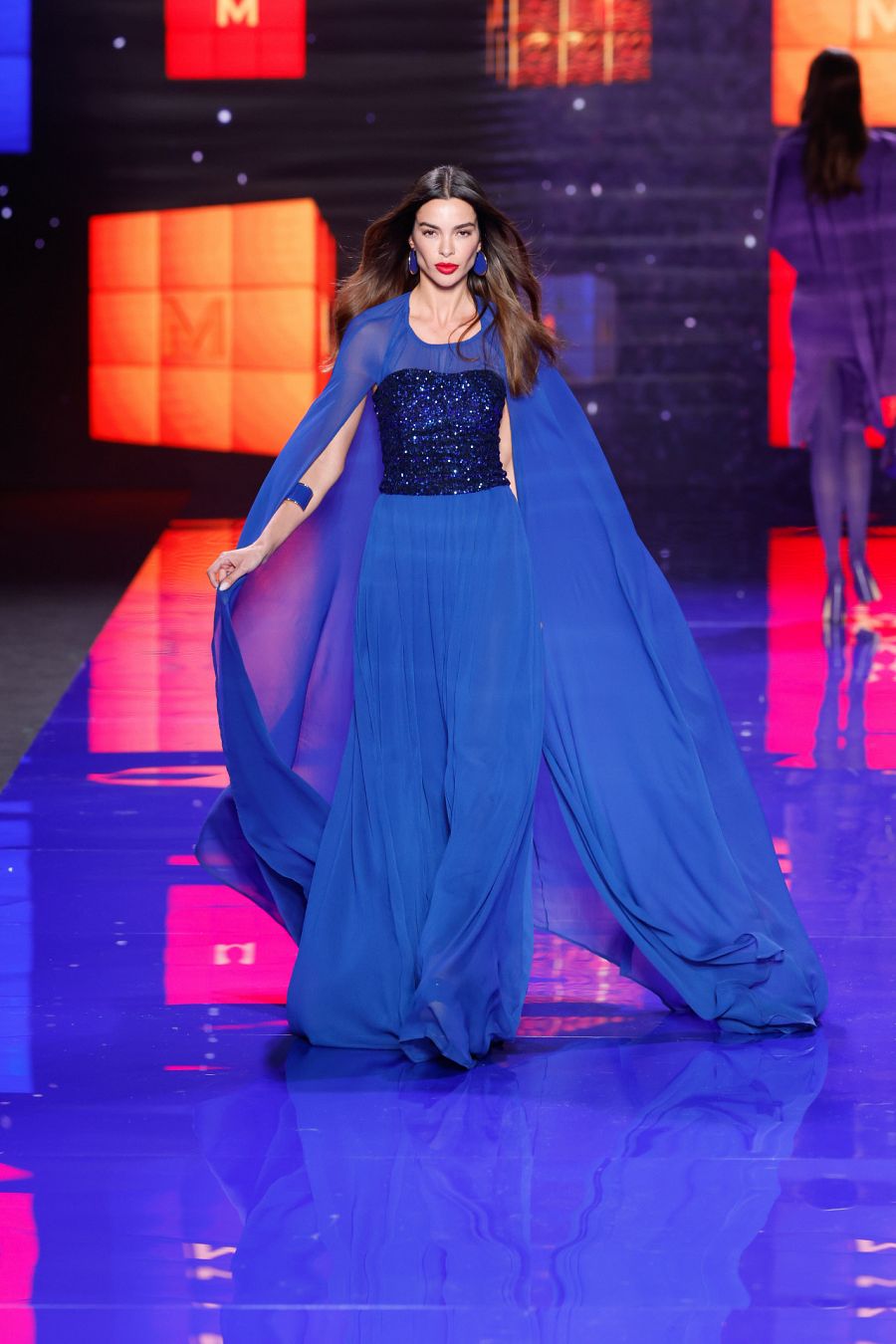 Joana Sanz en el desfile de Lola Casademunt by Maite con un largo vestido azul eléctrico con capa