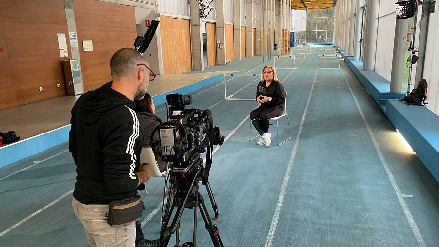 Operador de cámara entrevistando a María José Martínez Patiño en una pista de atletismo cubierta