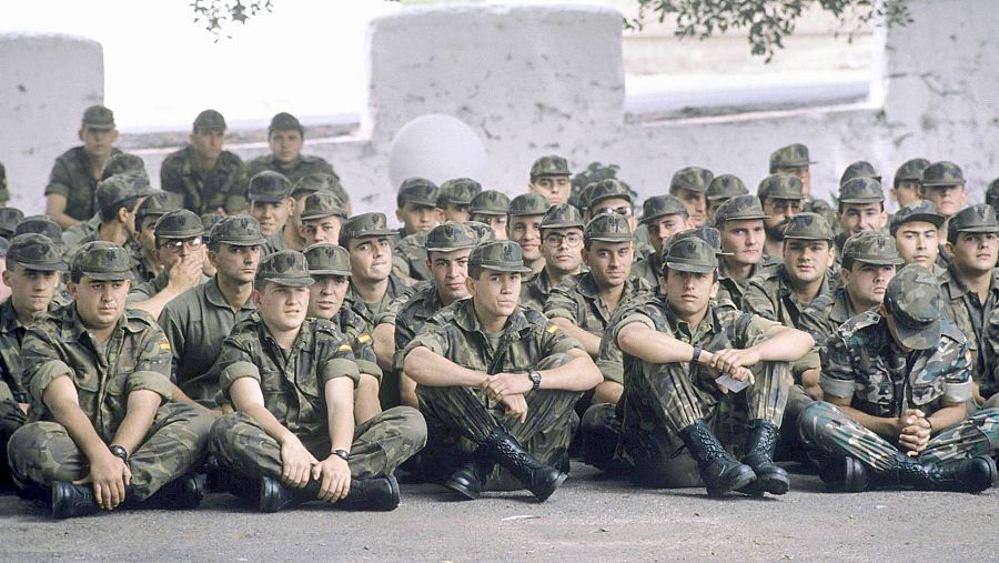 Soldados de reemplazo sentados en el suelo y vestidos con el uniforme militar recibiendo instrucción