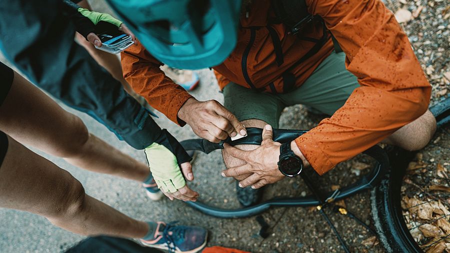 Álvaro Sanz arregla una punxada a la roda de la seva bicicleta sota la pluja i envoltat d'alguns companys